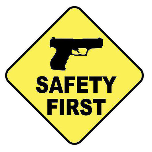 Yellow diamond-shaped sign featuring a black silhouette of a handgun above the bold text "SAFETY FIRST," emphasizing firearm safety awareness.