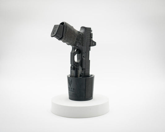 Black handgun securely placed in a Vets Tactical Cupolster, a cup holder-style holster designed for vehicle use, displayed on a white circular platform with a plain background.
